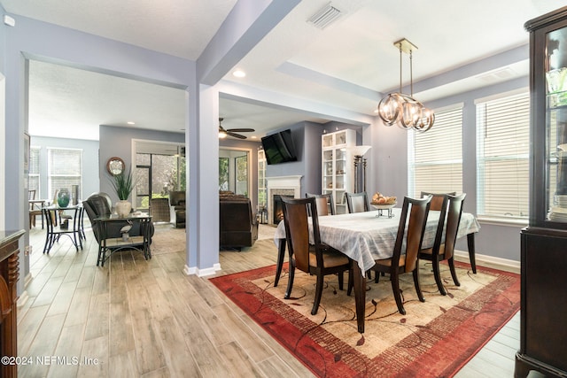 dining area featuring ceiling fan with notable chandelier, a tray ceiling, and light hardwood / wood-style flooring