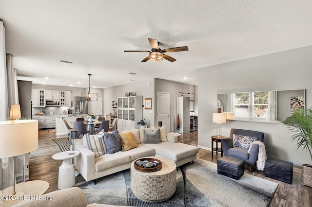 living room with a textured ceiling, ceiling fan, and dark wood-type flooring