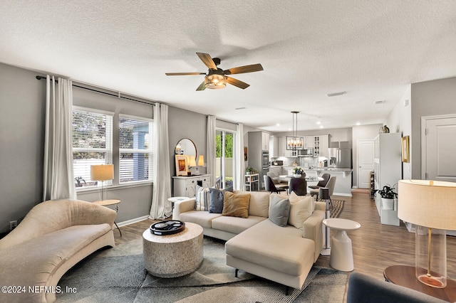 living room featuring ceiling fan with notable chandelier, a textured ceiling, and hardwood / wood-style flooring