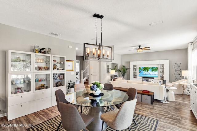 dining room with ceiling fan with notable chandelier, dark wood-type flooring, and a textured ceiling