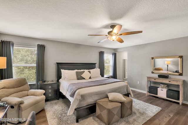 bedroom with a textured ceiling, ceiling fan, dark wood-type flooring, and multiple windows