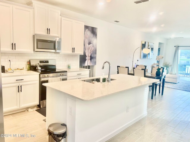 kitchen featuring light wood-type flooring, stainless steel appliances, a kitchen island with sink, sink, and white cabinets