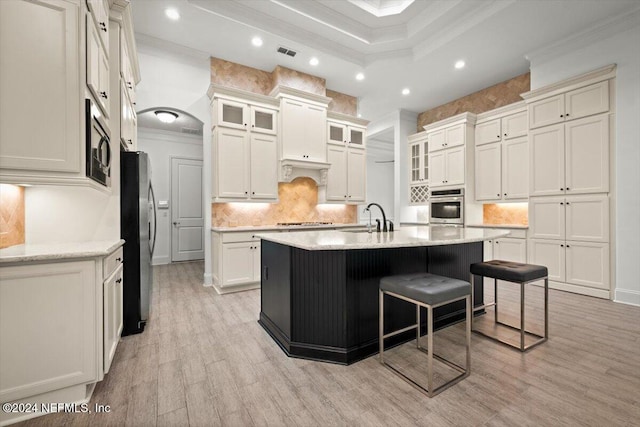 kitchen with a center island with sink, a kitchen bar, ornamental molding, light hardwood / wood-style floors, and stainless steel appliances