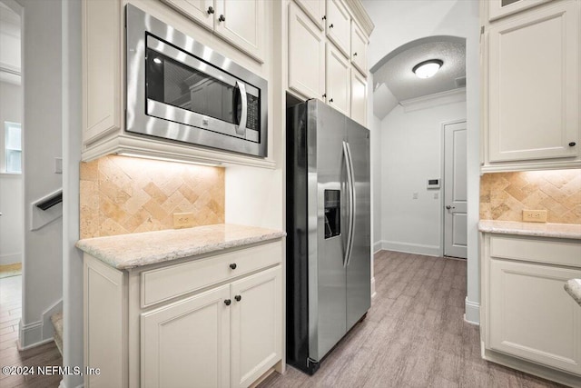 kitchen with a textured ceiling, light hardwood / wood-style floors, stainless steel appliances, light stone counters, and ornamental molding