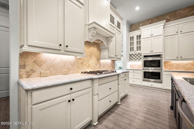 kitchen featuring decorative backsplash, appliances with stainless steel finishes, white cabinetry, light wood-type flooring, and light stone counters