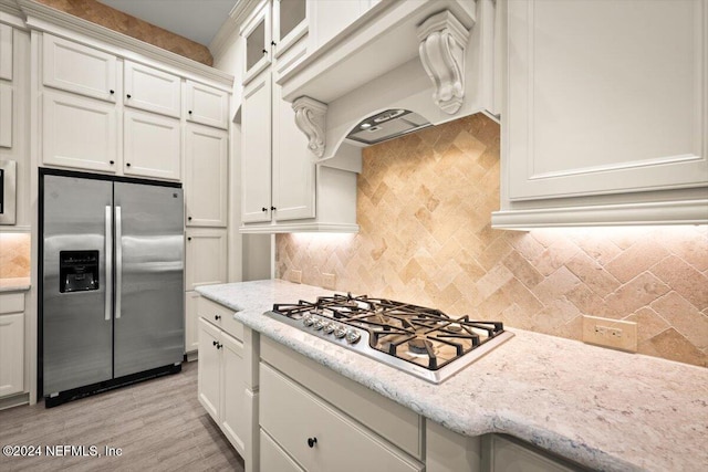 kitchen featuring decorative backsplash, appliances with stainless steel finishes, white cabinetry, light hardwood / wood-style flooring, and custom range hood