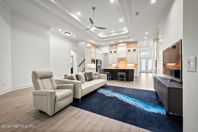 living room with crown molding, a tray ceiling, light hardwood / wood-style flooring, and ceiling fan