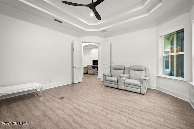 living area with ceiling fan, crown molding, a tray ceiling, and light hardwood / wood-style floors