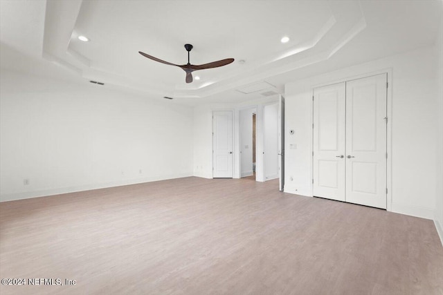 unfurnished bedroom with ceiling fan, a raised ceiling, and light hardwood / wood-style floors