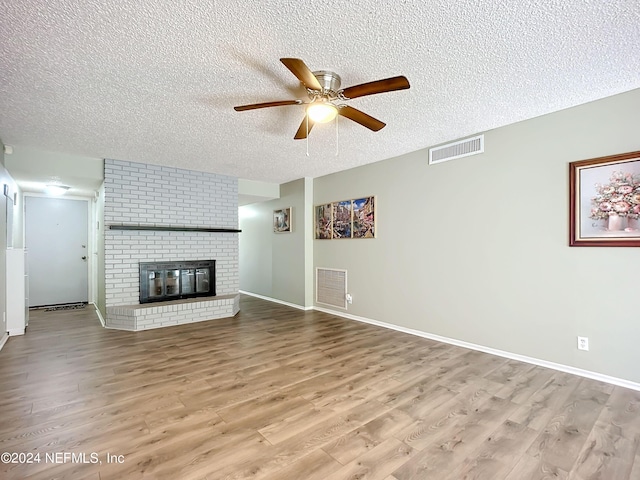 unfurnished living room with ceiling fan, a textured ceiling, light wood-type flooring, and a fireplace