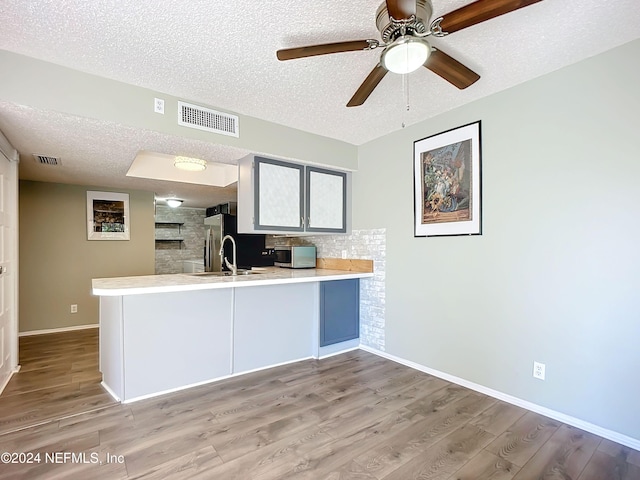 kitchen featuring sink, light wood-type flooring, a textured ceiling, kitchen peninsula, and ceiling fan