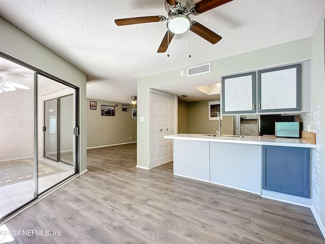 kitchen with ceiling fan, a textured ceiling, light hardwood / wood-style flooring, and kitchen peninsula