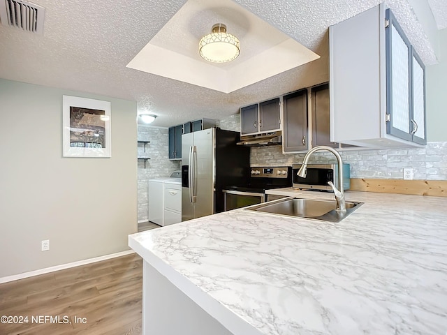 kitchen featuring kitchen peninsula, wood-type flooring, stainless steel range with electric cooktop, a raised ceiling, and a textured ceiling