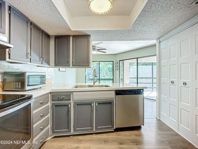 kitchen with sink, kitchen peninsula, ceiling fan, stainless steel appliances, and light hardwood / wood-style flooring