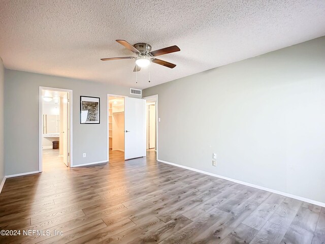 unfurnished bedroom with hardwood / wood-style flooring, a closet, a walk in closet, a textured ceiling, and ceiling fan