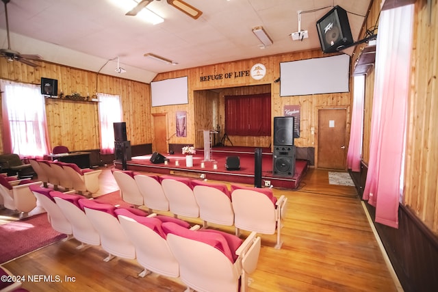 cinema room featuring ceiling fan, wood walls, and hardwood / wood-style floors