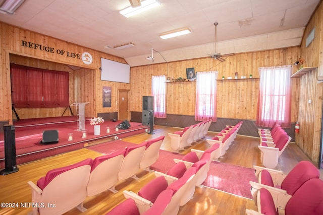 home theater room featuring hardwood / wood-style flooring, wood walls, lofted ceiling, and ceiling fan