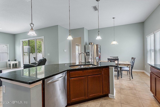 kitchen with appliances with stainless steel finishes, a kitchen island with sink, light tile patterned flooring, sink, and decorative light fixtures