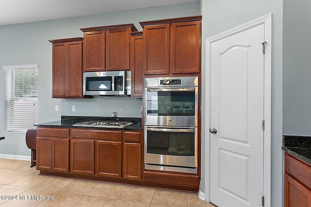 kitchen with appliances with stainless steel finishes, dark stone countertops, and light tile patterned flooring