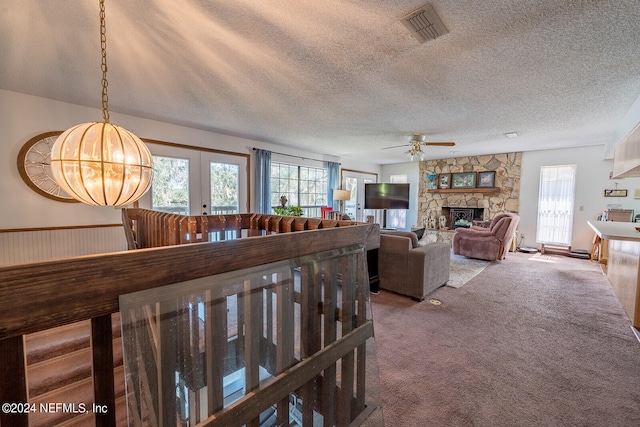 carpeted living room featuring french doors, ceiling fan, a stone fireplace, and a textured ceiling