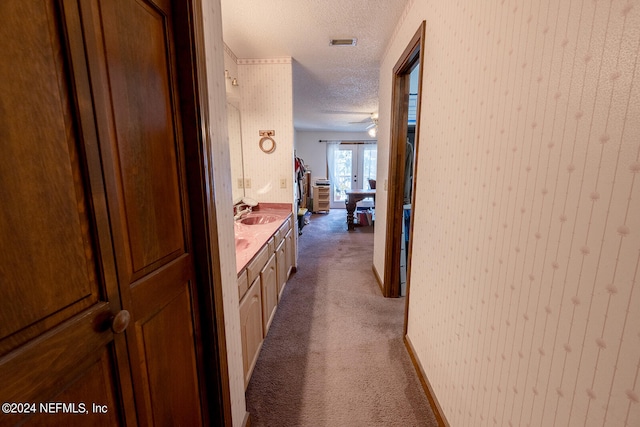 corridor with a textured ceiling, sink, and dark carpet