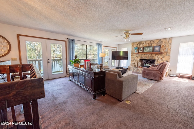 carpeted living room featuring french doors, ceiling fan, a textured ceiling, and a fireplace