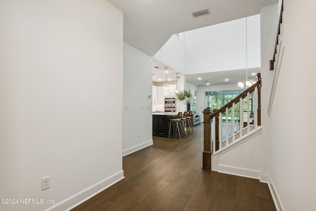 corridor with a towering ceiling, a notable chandelier, and dark hardwood / wood-style floors