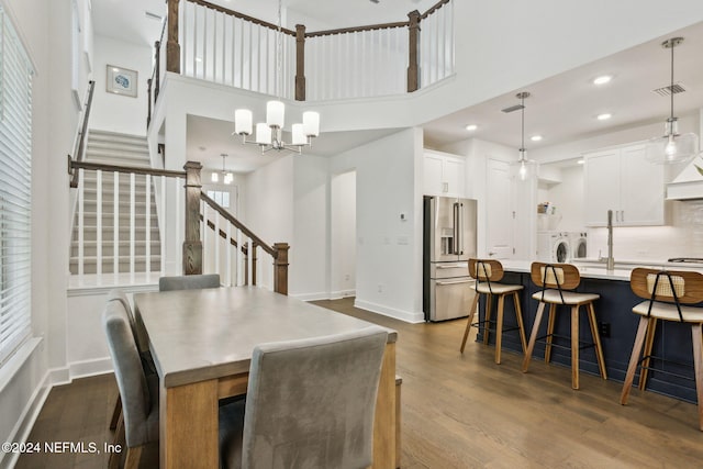 dining room featuring a high ceiling, washer and clothes dryer, a notable chandelier, and hardwood / wood-style flooring