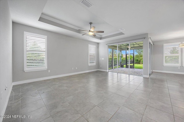 empty room with light tile patterned flooring, ceiling fan, a healthy amount of sunlight, and a raised ceiling