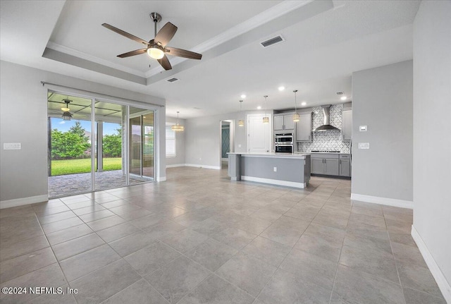 unfurnished living room featuring crown molding, a tray ceiling, light tile patterned floors, and ceiling fan