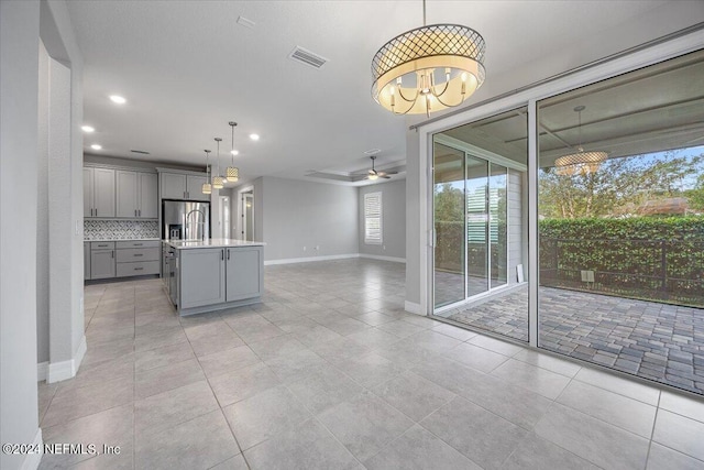 kitchen featuring ceiling fan, an island with sink, gray cabinetry, stainless steel refrigerator with ice dispenser, and decorative light fixtures