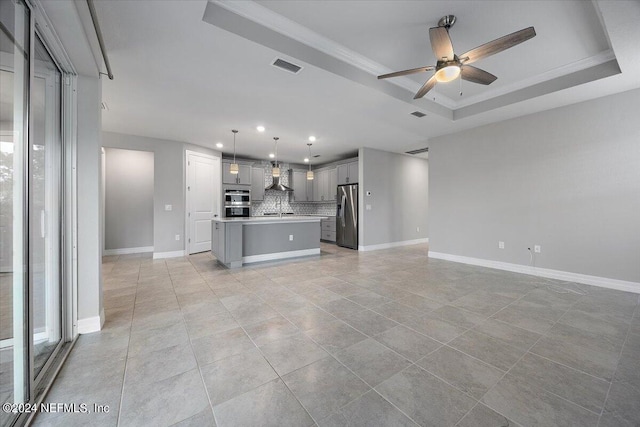 kitchen featuring wall chimney range hood, gray cabinetry, a center island, a raised ceiling, and appliances with stainless steel finishes