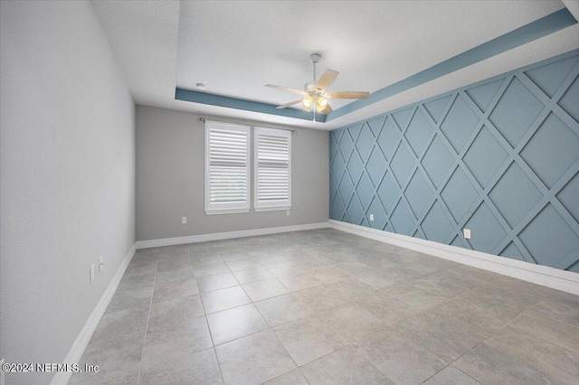 unfurnished room with ceiling fan, light tile patterned flooring, and a tray ceiling