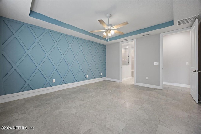 unfurnished bedroom with light tile patterned flooring, a tray ceiling, and ceiling fan