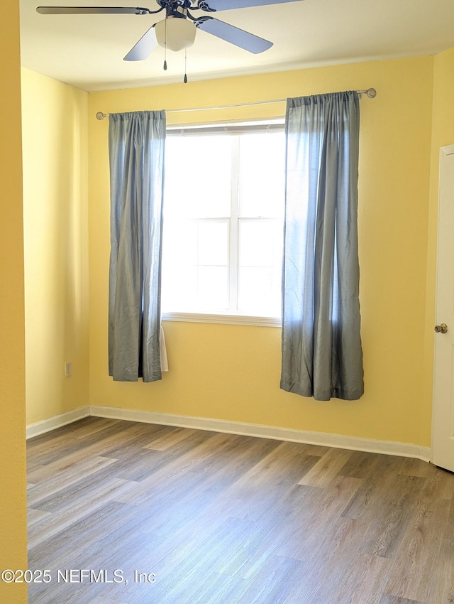 empty room with wood finished floors, a ceiling fan, and baseboards