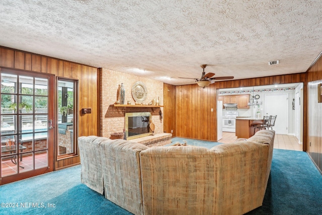 living room with ceiling fan, a textured ceiling, a fireplace, light colored carpet, and wooden walls