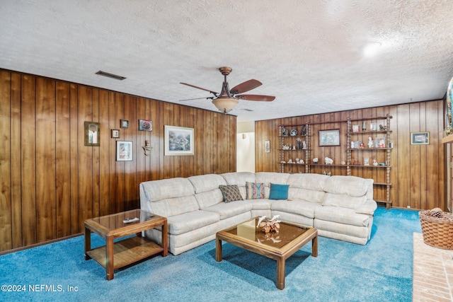 carpeted living room with wood walls, ceiling fan, and a textured ceiling