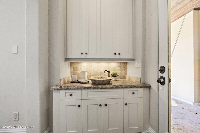 bar with white cabinets, backsplash, and dark stone countertops