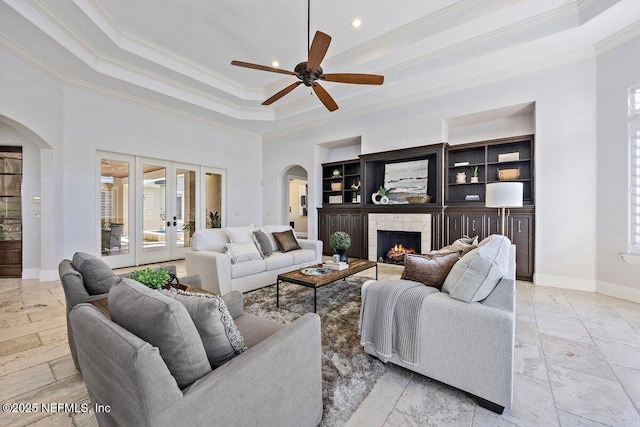 living room with ceiling fan, french doors, a raised ceiling, a stone fireplace, and ornamental molding