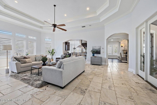 living room with a towering ceiling, a tray ceiling, ceiling fan, and ornamental molding