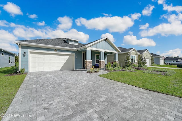 craftsman house featuring board and batten siding, stone siding, decorative driveway, a front lawn, and a garage