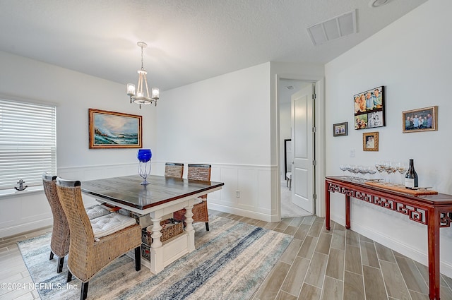 dining room with a chandelier, visible vents, wood finish floors, and wainscoting