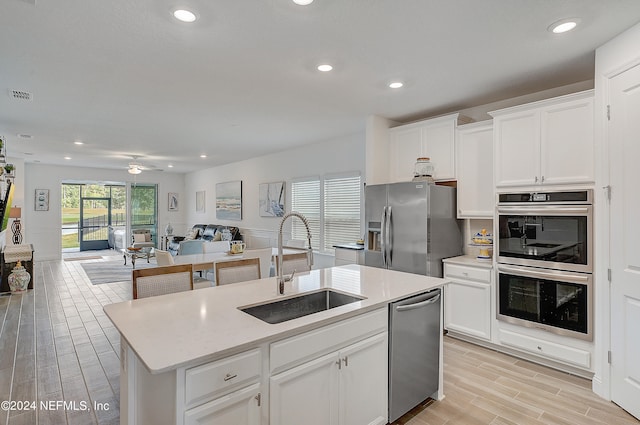 kitchen with white cabinets, an island with sink, light hardwood / wood-style flooring, sink, and stainless steel appliances