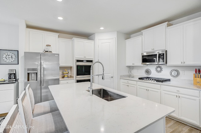 kitchen with white cabinetry, a kitchen island with sink, light wood-type flooring, sink, and stainless steel appliances