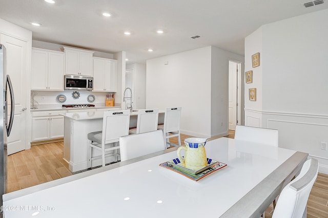 kitchen featuring light hardwood / wood-style floors, white cabinetry, a center island with sink, and a breakfast bar area