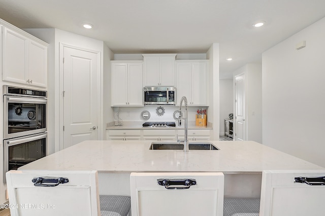 kitchen featuring white cabinetry, stainless steel appliances, sink, and an island with sink