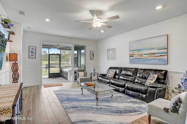 living room with a textured ceiling, light hardwood / wood-style floors, and ceiling fan