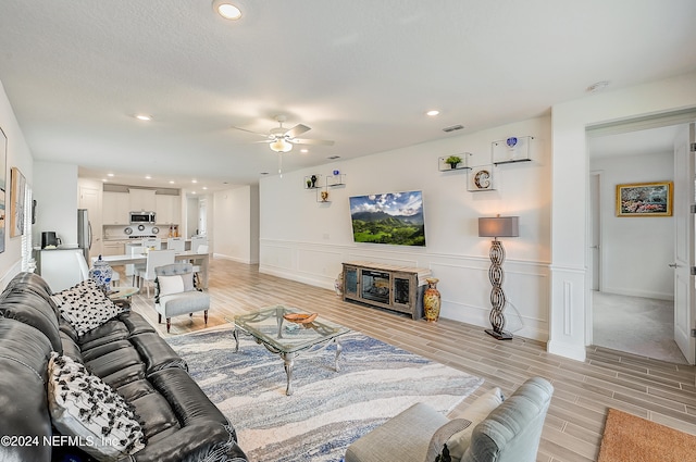 living room featuring light hardwood / wood-style floors, a textured ceiling, and ceiling fan