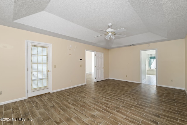 unfurnished room with ceiling fan, a raised ceiling, a textured ceiling, and dark hardwood / wood-style flooring