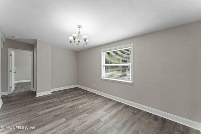 spare room featuring a textured ceiling, hardwood / wood-style flooring, and an inviting chandelier